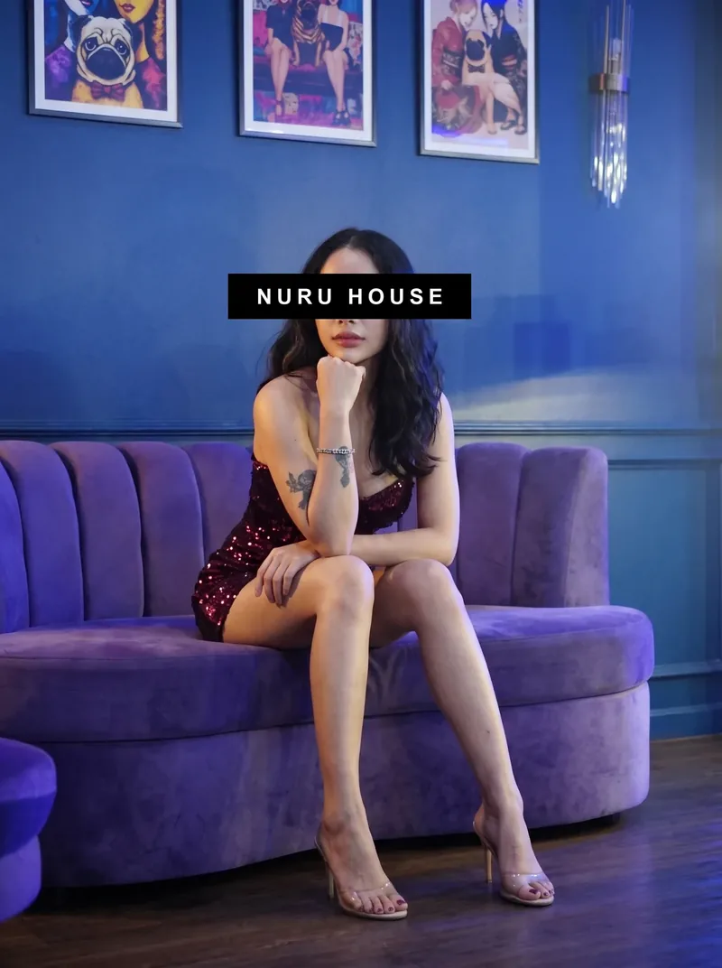 Sitting on the edge of a purple velvet sofa in a dark sequined mini dress, framed prints on the blue wall