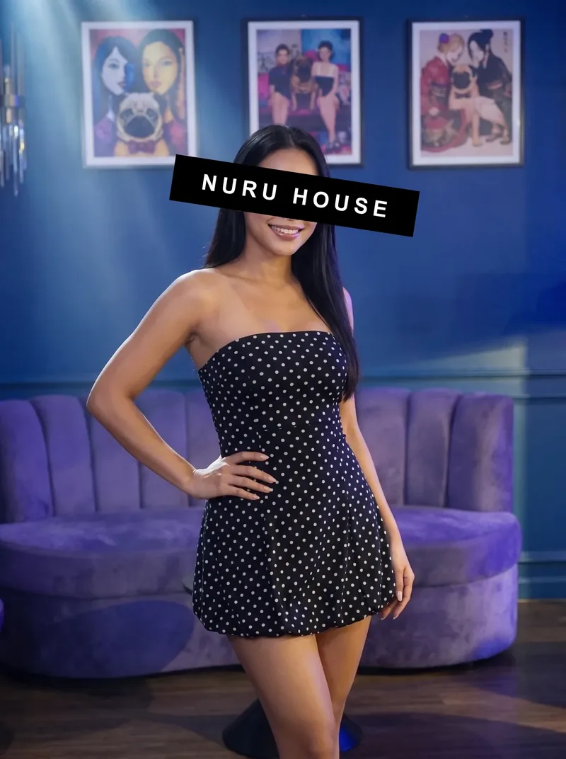 Standing by the velvet sofa in a black polka-dot strapless dress, hands on hips