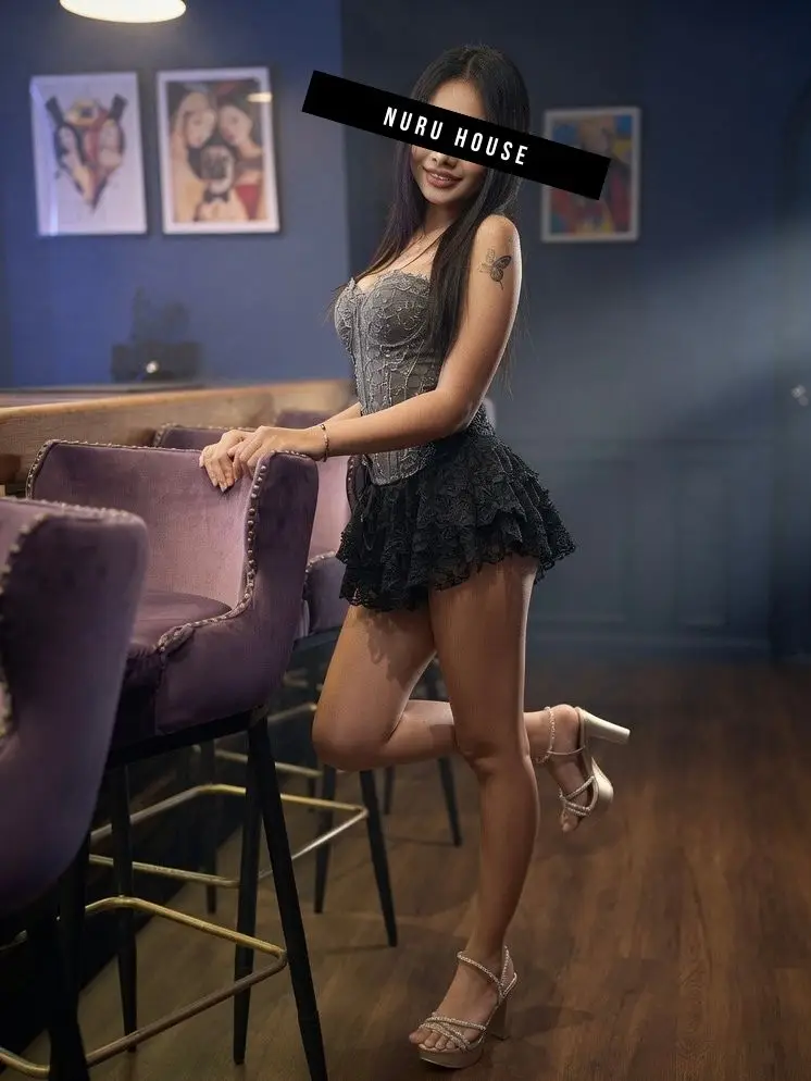 Perched on a bar stool in a black lace mini dress, one heel resting on the footrest