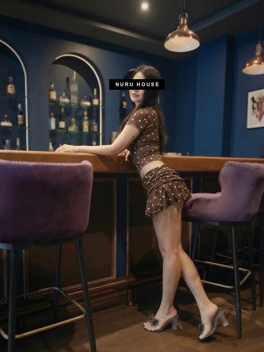 Leaning on the bar counter in a leopard-print two-piece, bottles on the shelves behind